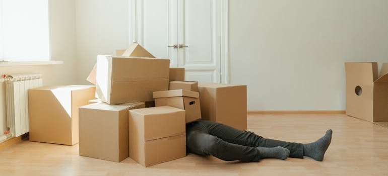 a man under a bunch of boxes thinking about how to downsize your belongings before a move/