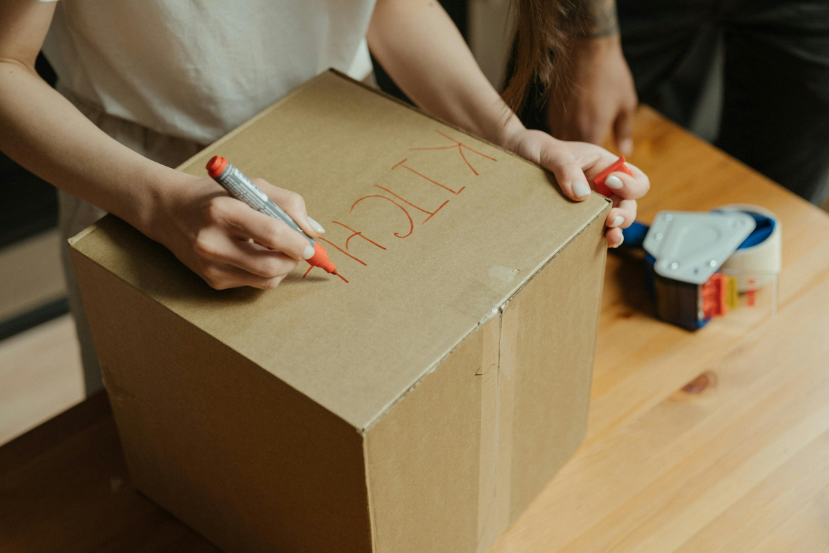 person writing "kitchen" on a cardboard box