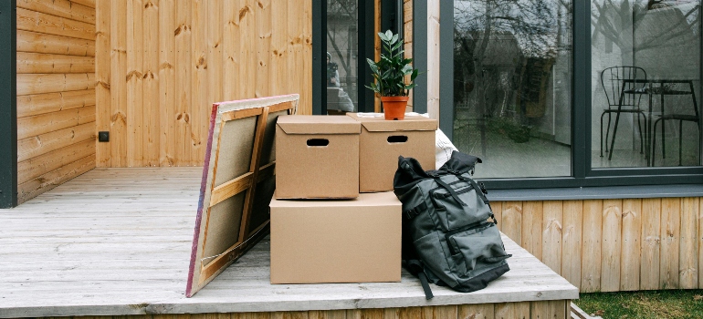 Boxes and a backpack neatly arranged on a wooden porch, preparing for transportation.