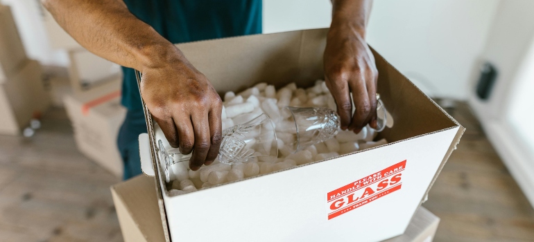 Close-up of hands safely packing glassware into a moving box, showing how to pack fragile items when moving.