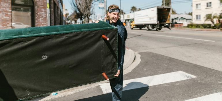 Smiling mover carrying a green couch on a sidewalk, illustrating commercial moving companies atlanta ga in action.