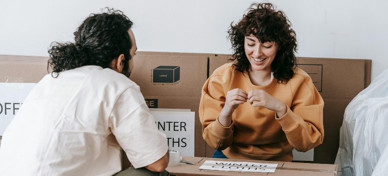 A couple smiling while organizing and labeling boxes in preparation for a move.