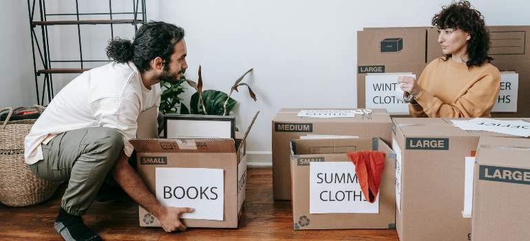 A couple organizing boxes labeled 'Books' and 'Summer Clothes,' preparing for a move.