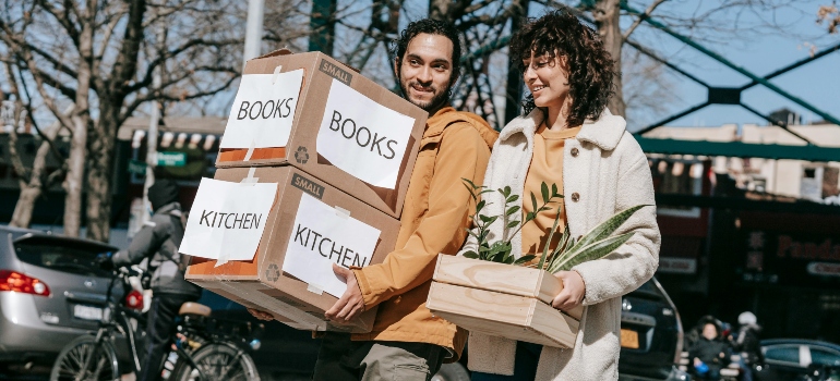 A couple carrying labeled boxes outdoors during a move, showcasing the process of moving your family from a house to an apartment.