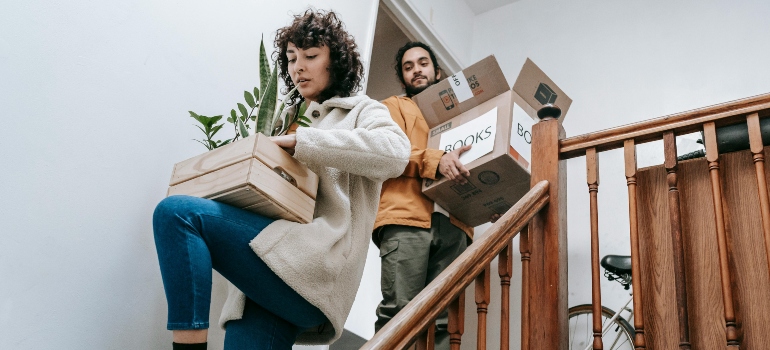 A couple moving boxes down the stairs, preparing for a big transition to a new house.