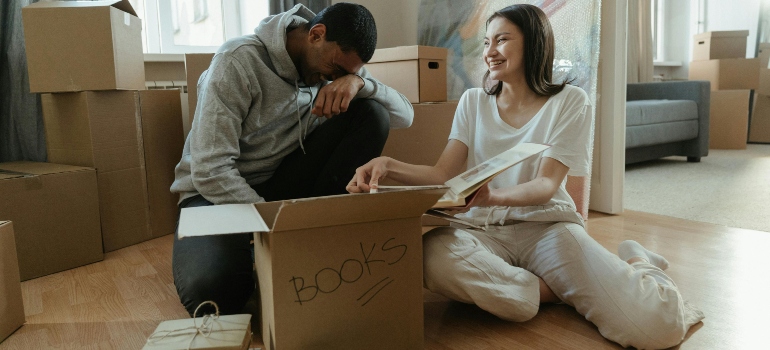 A couple sitting on the floor, sorting books into a box before moving.