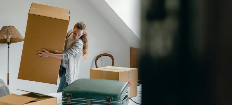 A person holding a large cardboard box, working with movers Lawrenceville GA, inside a neat and mostly empty space.