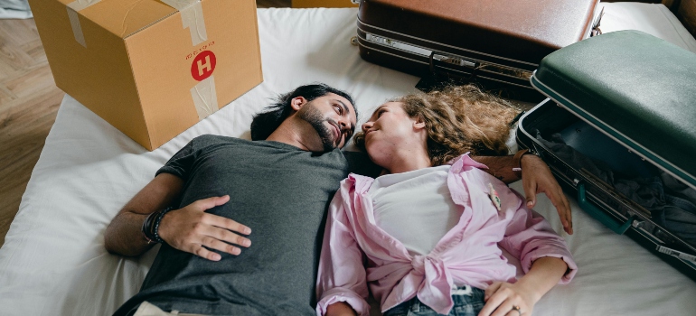 Couple lying on a bed, surrounded by moving boxes, sharing a moment of joy during their move.