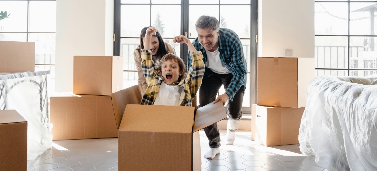 A family playing and laughing with moving boxes in a sunlit room after moving to Atlanta.