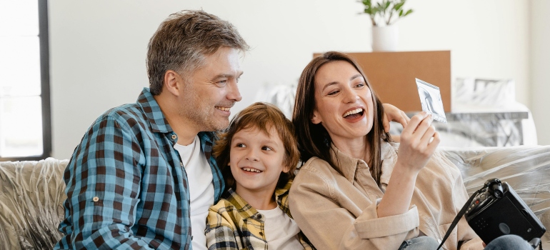 A smiling family sitting on a couch, holding a picture and preparing for their upcoming move with movers Woodstock GA.