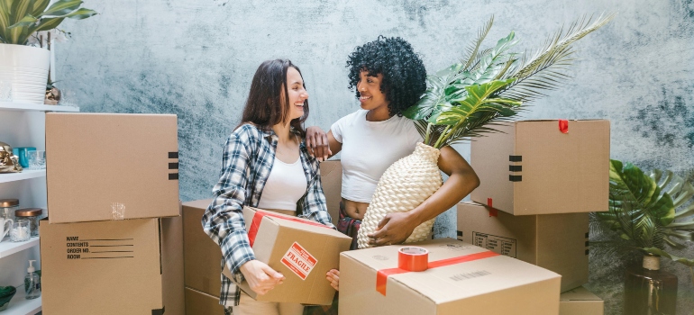 Two people smiling and holding packing boxes, planning their move.