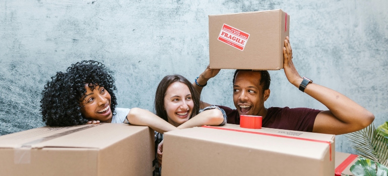 Three people laughing behind stacked boxes, keeping their move organized.