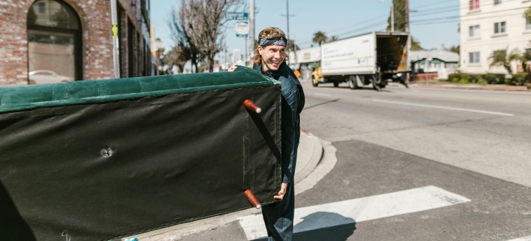 A skilled mover carrying a green sofa safely during a relocation with movers Fayetteville GA.