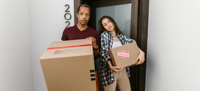 A man and a woman holding boxes near a door.