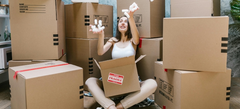 A person sits amid boxes and tosses packing materials in the air, illustrating movers Suwanee GA reliability.