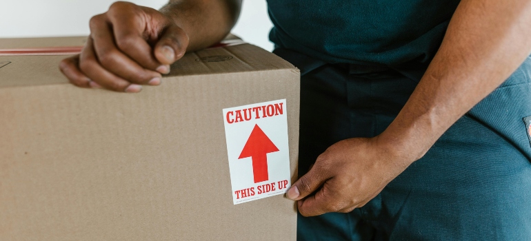 Close-up of a mover holding a box with a 'Caution: This Side Up' label.