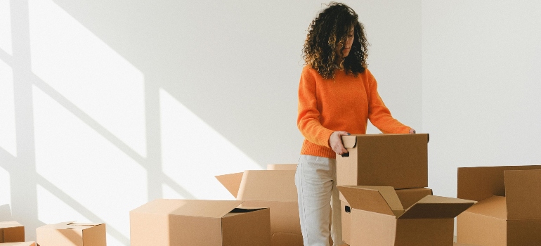 Woman organizing and lifting cardboard boxes during a move, providing tips for moving out for the first time.