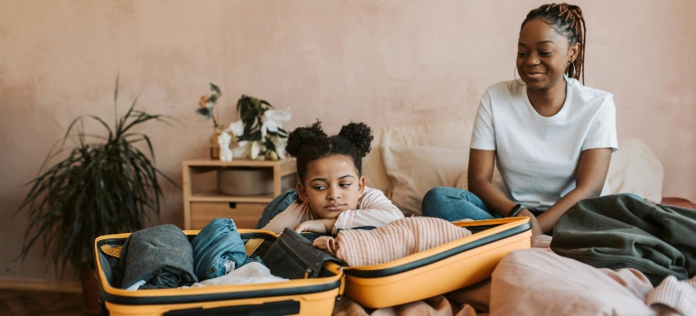 A mother and her daughter packing clothes into a suitcase, sharing a moment during their family move.