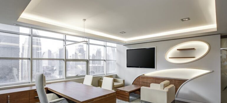 Gray Office Rolling Chair Near Brown Wooden Desk in Front of Flat Screen Tv on White Painted Wall