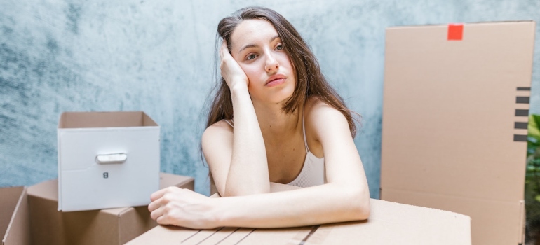 a worried woman sitting next to moving boxes before moving out last minute